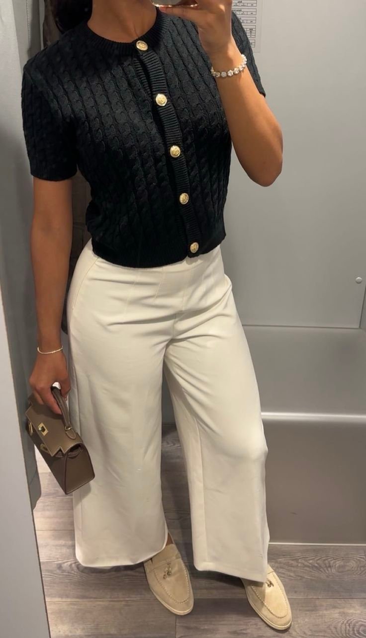 Femme portant le gilet crop Sorrente Riviera en maille torsadée noire avec boutons dorés.